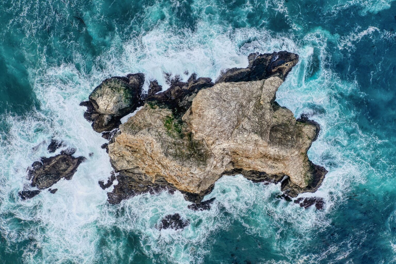 Ocean waves surrounding a rocky island, viewed from above.