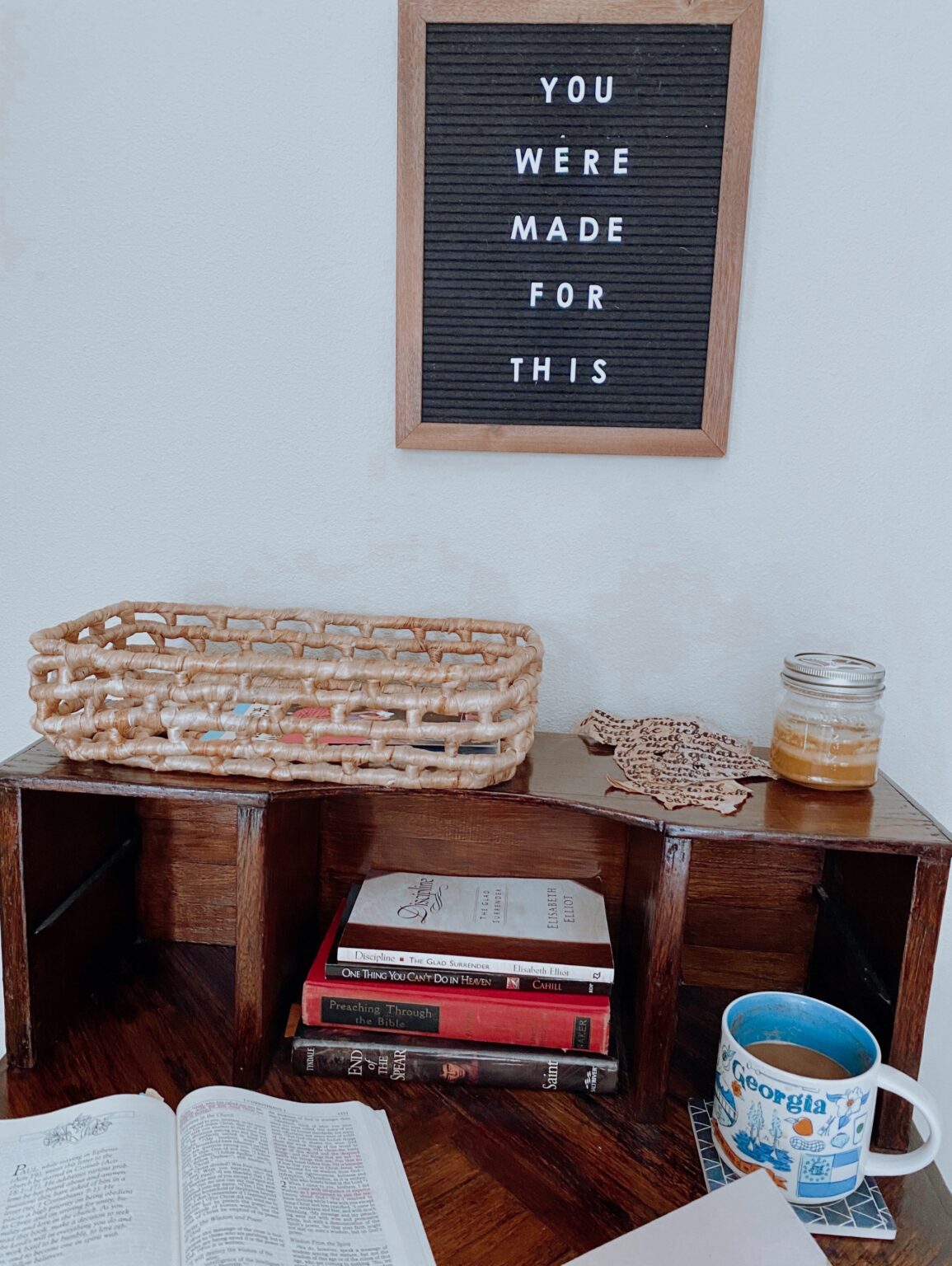 An open Bible and cup beside a stack of books, beneath a sign reading “You were made for this.”